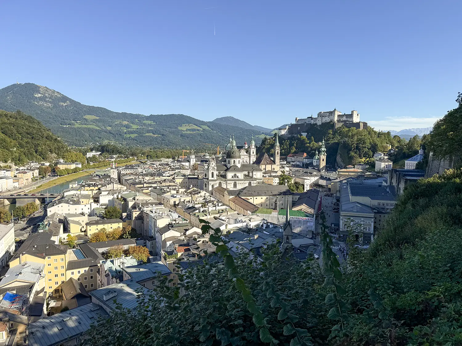Landscape view looking across the rooftops of Salzburg, Austria. In the distance a castle perches over the city from the top of a hill.